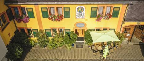 Ein gelbes Gebäude mit grünen Fensterläden, eine Schilder mit der Aufschrift "Conferin's Eis Bar" und eine Terrasse mit Sonnenschirmen.