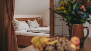 A hotel room with a bed, a nightstand with a vase of flowers, and a fruit bowl. - KultUrlaub Mosel GbR (Kröv)