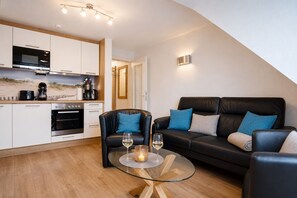 A modern living space with a kitchen, a leather sofa, a glass coffee table, and a dining area.