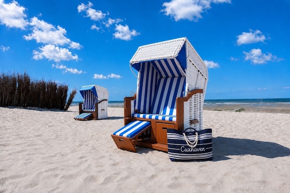 Beach chairs with striped cushions and a beach bag labeled 'Cuxhaven' on a sandy beach.