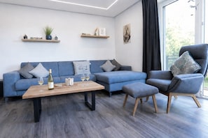 Uma sala de estar moderna com um sofá azul, uma mesa de centro de madeira e uma poltrona cinza.