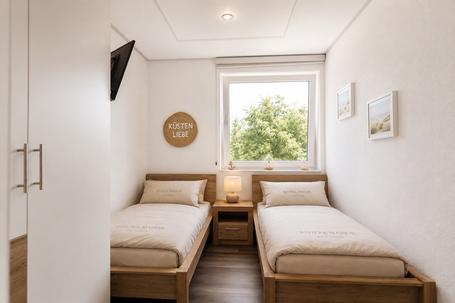 A bedroom with two beds, a window with a view of trees, a wall-mounted TV, and a circular sign with text.