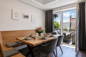 Uma sala de jantar com mesa de madeira posta para quatro pessoas, cadeiras estofadas cinzas, um vaso com flores e quadros nas paredes.