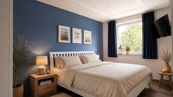 Une chambre à coucher comprenant un lit, des tables de chevet, une commode, une lampe, une fenêtre avec des rideaux et des œuvres d’art murales.