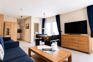 Una sala de estar moderna con un sofá, una mesa de comedor, un televisor y una zona de cocina.