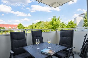 Un balcon avec trois chaises noires, une table et deux verres de vin blanc.