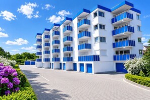 Un immeuble à plusieurs étages doté de balcons, d’une allée pavée et entouré de verdure.