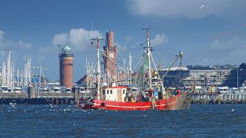 A harbor with a large fishing boat, a clock tower, and a lighthouse in the background.