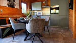 Ein Holzinterieur mit Esstisch, Stühlen, einer Küche inklusive Herd und Kühlschrank.