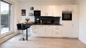 A modern kitchen with white cabinets, a black countertop, and a black chair. - Vacation apartment Cuxhaven-Döse-Duhnen near the beach with sauna, south-facing terrace & beach chair (Cuxhaven)
