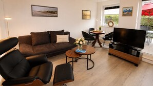 A modern living room with a sofa, chairs, a coffee table, a TV, and artwork on the walls. - Vacation apartment Cuxhaven-Döse-Duhnen near the beach with sauna, south-facing terrace & beach chair (Cuxhaven)