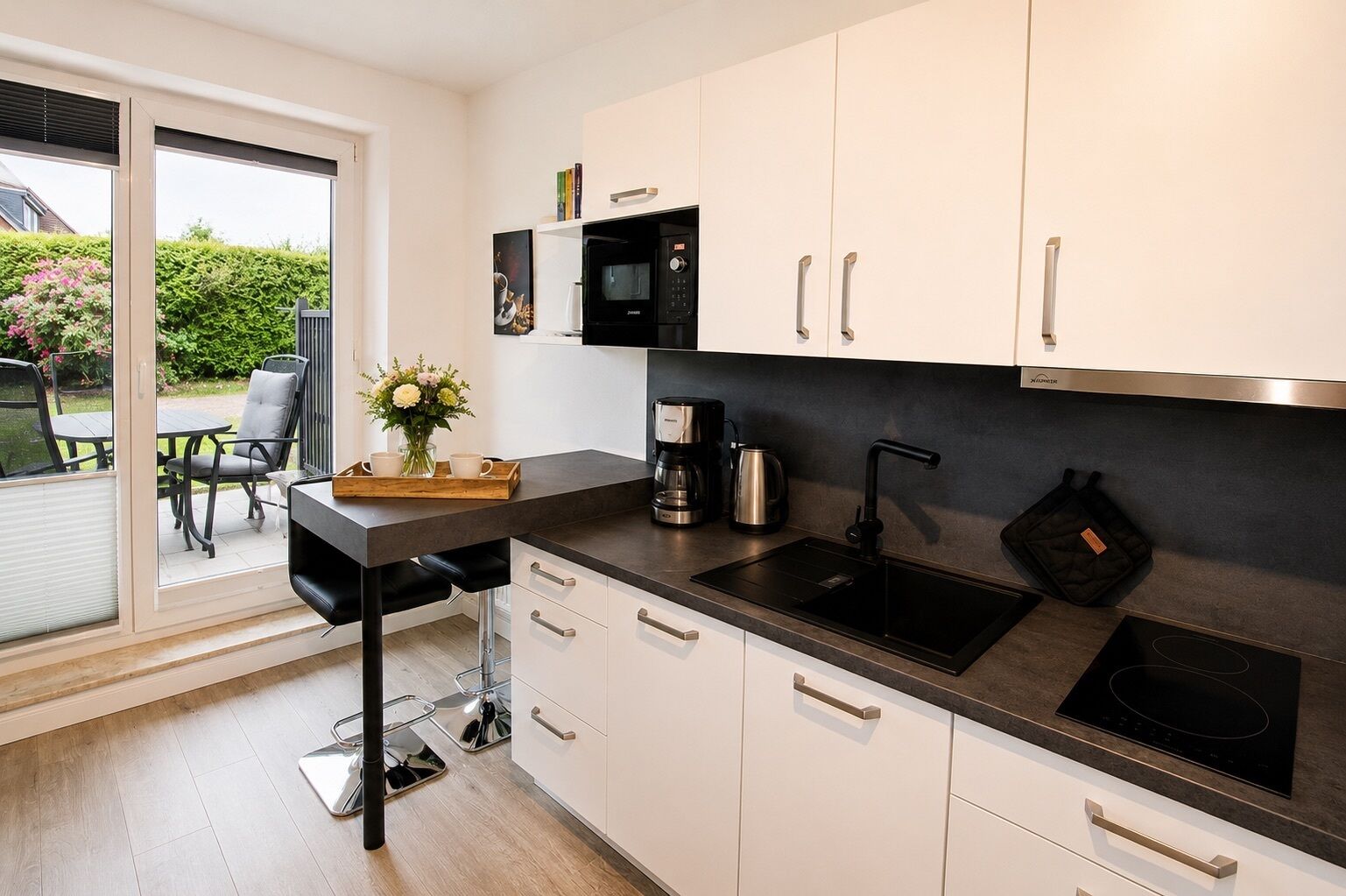 Una cucina moderna con un piano di lavoro nero, mobili bianchi, forno integrato e macchina per il caffè.