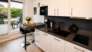 A modern kitchen with a black countertop, white cabinets, a built-in oven, and a coffee maker. - Vacation apartment Cuxhaven-Döse-Duhnen near the beach with sauna, south-facing terrace & beach chair (Cuxhaven)