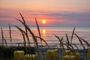 Ein Strandbild mit Stühlen und einem Sonnenuntergang.