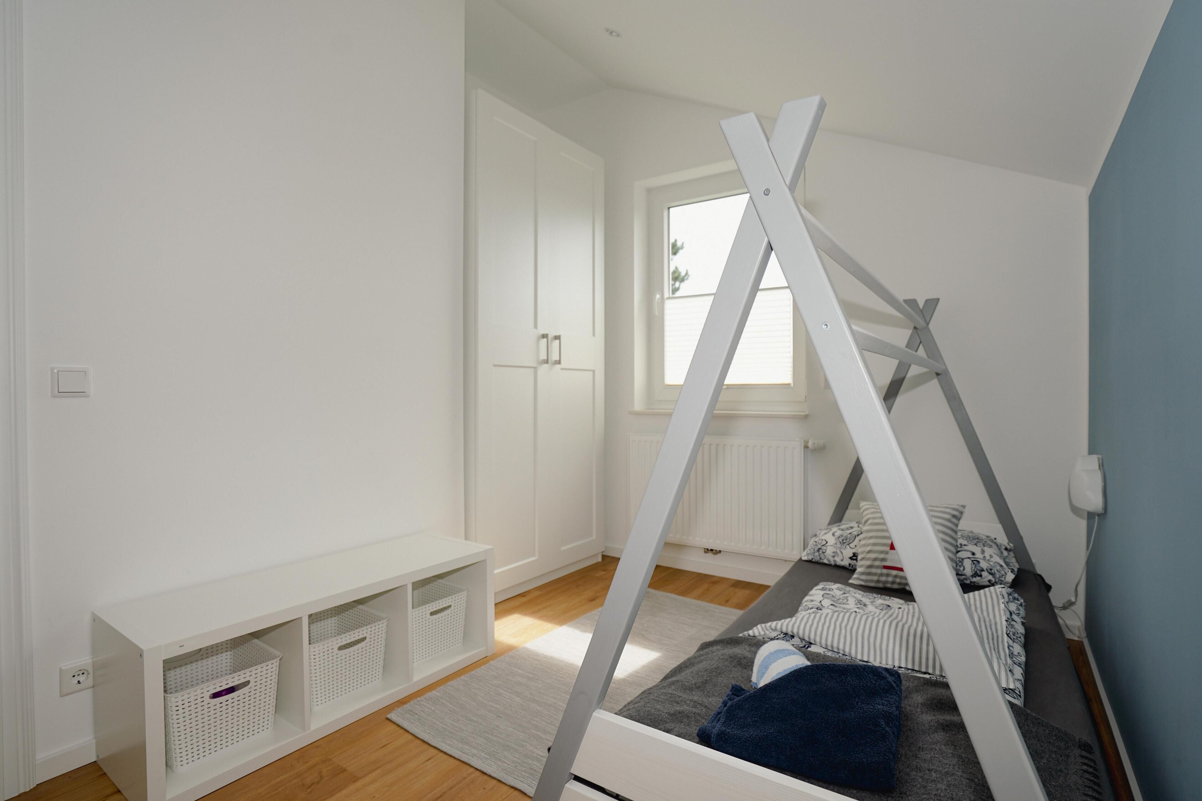 A bedroom with a bed, a white wardrobe, a window, and storage shelves.