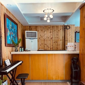 Een receptiezone met een wand van houten panelen, een piano, een koelkast en een beeld.