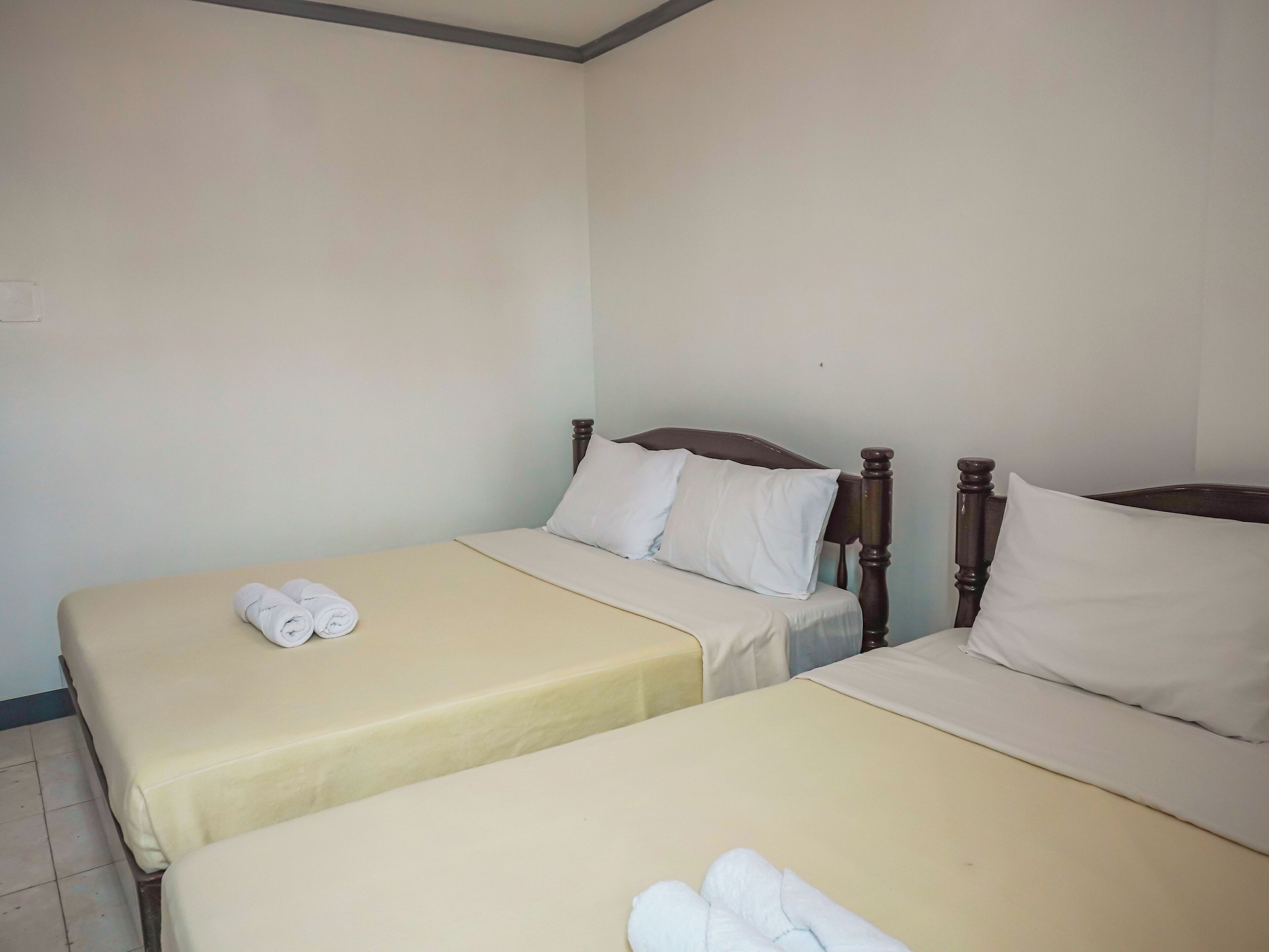 A room with two single beds, each with a wooden headboard and white bedding.