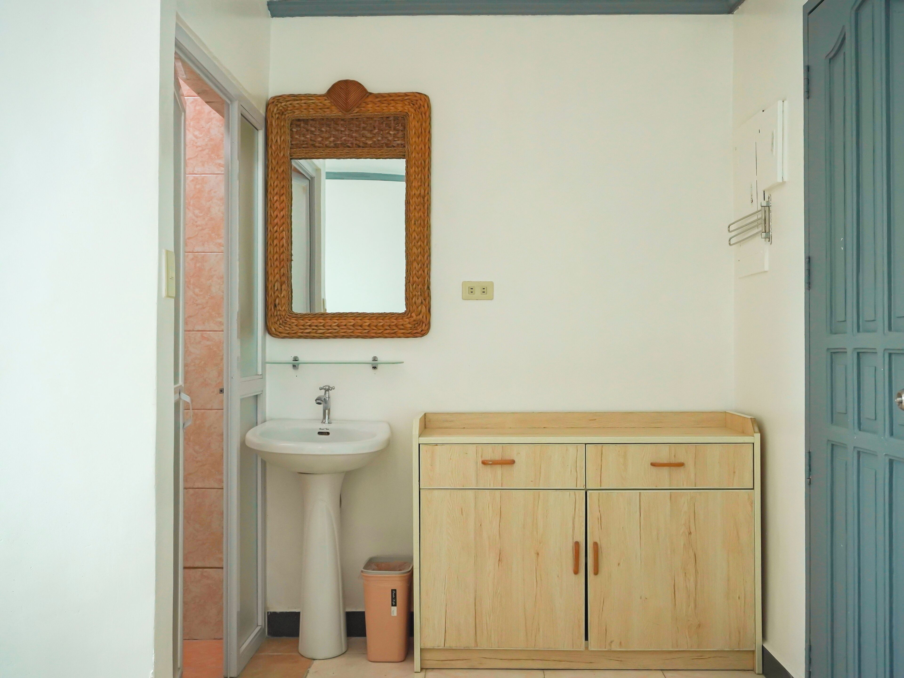 Un baño con un lavabo blanco, un armario de madera y un espejo con marco de mimbre.