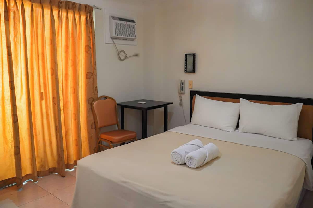Ein Hotelzimmer mit Bett, Sessel, kleinem Tisch, Klimaanlage und Telefon.