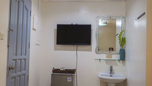 A bathroom with a grey door, a television mounted on the wall, a sink with a mirror, and a small refrigerator. - Boracay Paradise Hotel (Boracay Island)