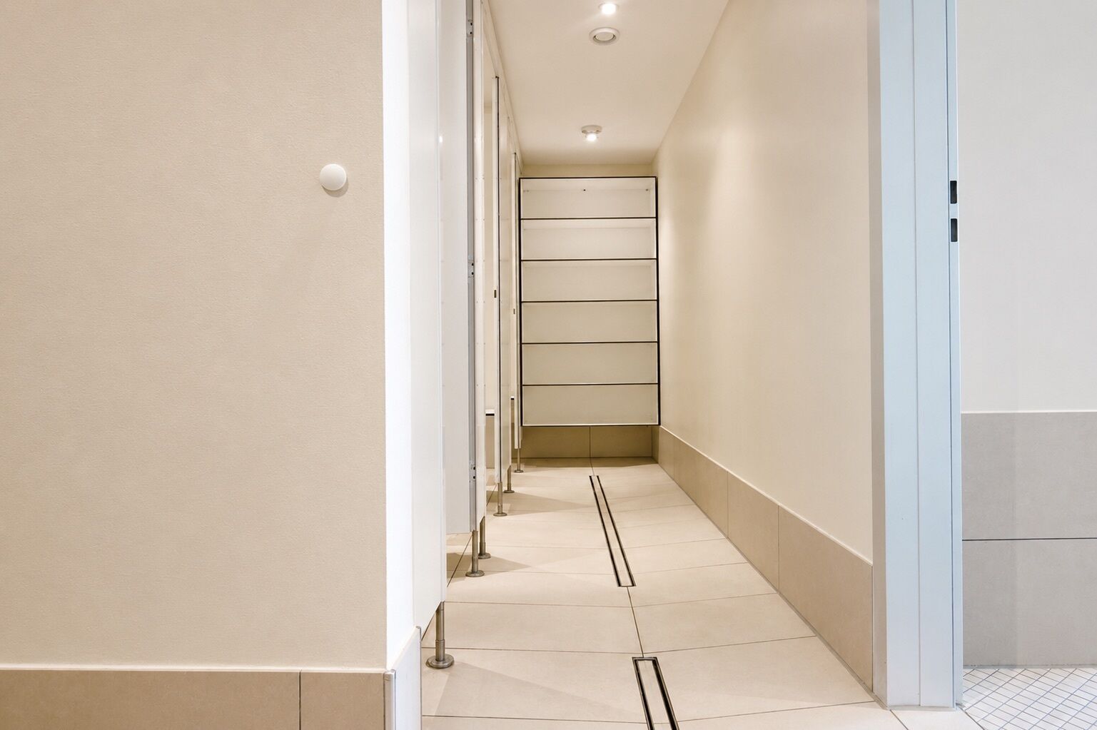 A modern hallway with a tiled floor, recessed lighting, and a door on the right.