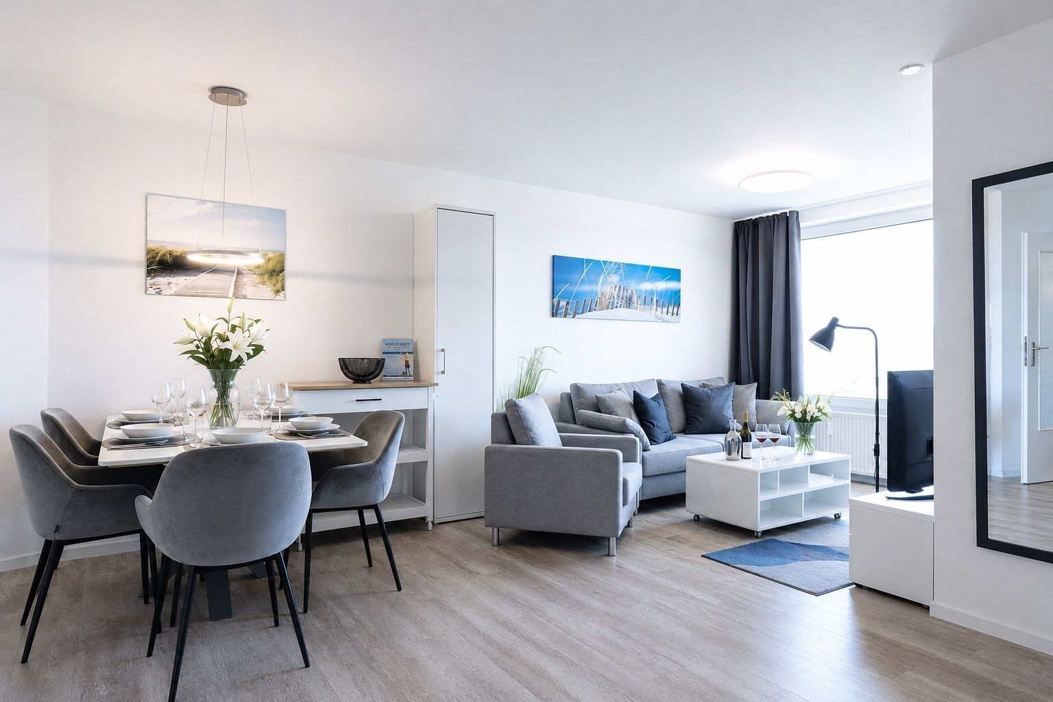 A modern living room with a dining area, grey sofas, a flat-screen TV, and artwork on the walls.