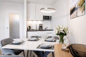 Una cocina moderna con microondas, cafetera y zona de comedor dispuesta con platos, vasos y un florero.