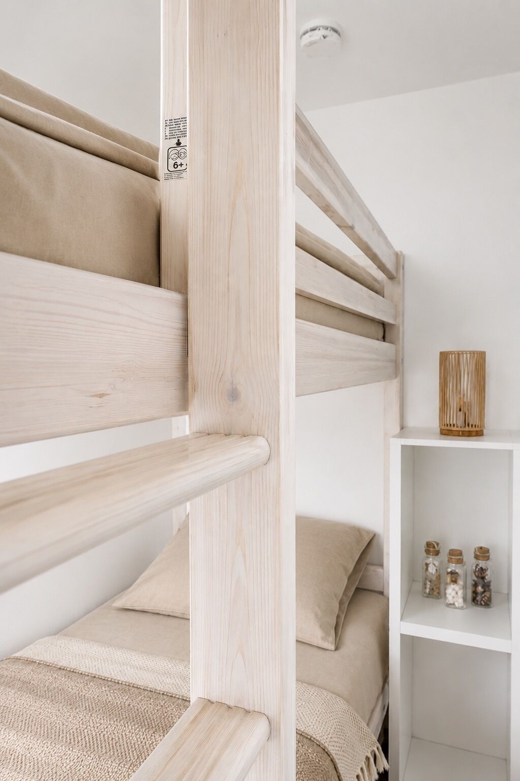 A bunk bed with a white headboard, a white shelf with jars, and a white wall.
