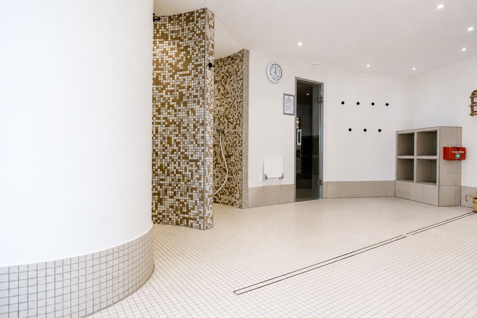 A clean, modern bathroom with a tiled floor, a shower area, a clock, and a fire extinguisher.