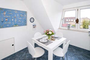 Ein Essbereich mit einem weiĂen Tisch, vier StĂŒhlen, einer Blumenvase, einer Uhr und einem Kalender an der Wand.