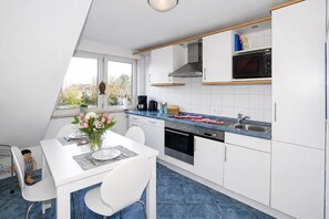 Eine moderne KĂŒche mit weiĂen SchrĂ€nken, einer blauen Arbeitsplatte und einem Essbereich mit weiĂem Tisch und StĂŒhlen.