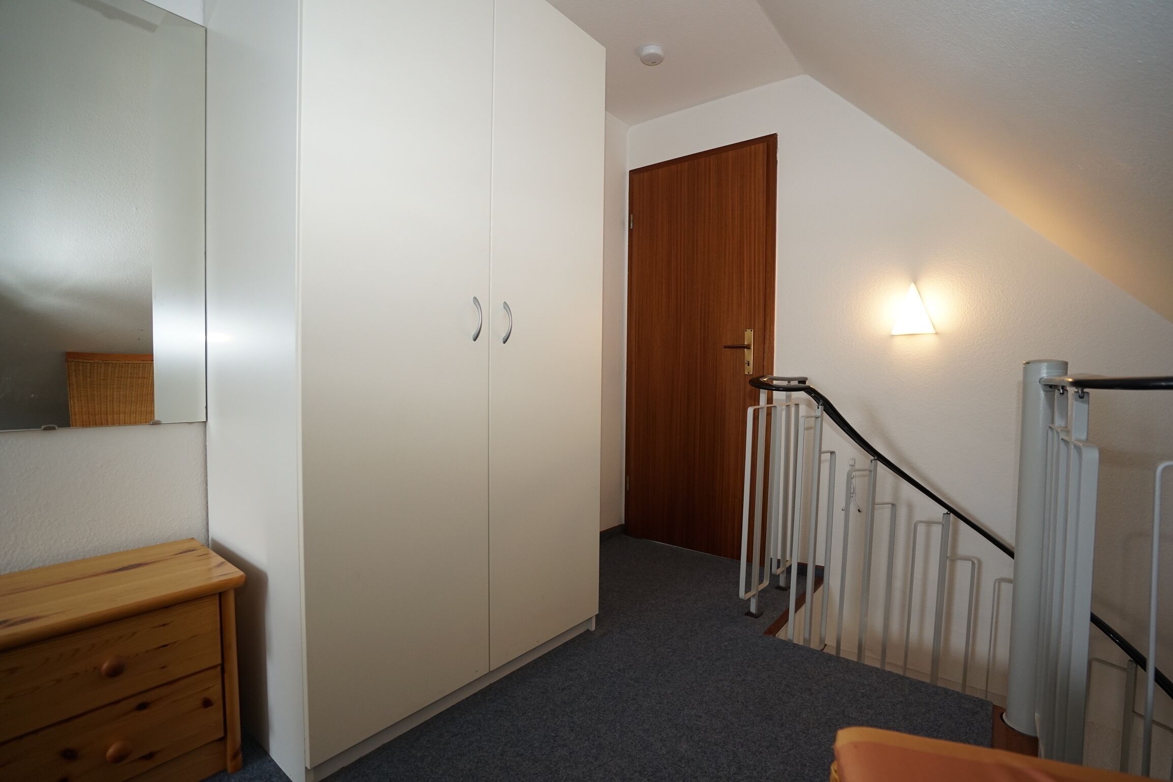 A bedroom with a wardrobe, a wooden door, a radiator, and a staircase.