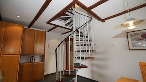 Un escalier en colimaçon avec des marches en bois et une rampe blanche, un meuble en bois avec des étagères et une table avec une chaise.