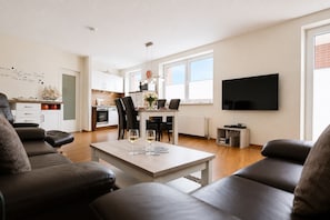Una sala de estar moderna con comedor, una cocina al fondo y un televisor de pantalla plana grande montado en la pared.