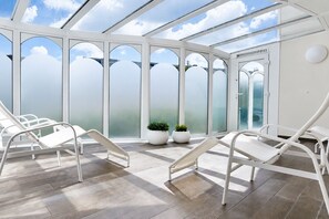 A conservatory with white metal chairs, a tiled floor, and potted plants.