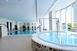 An indoor swimming pool with a separate hot tub area, tiled flooring, and large windows.
