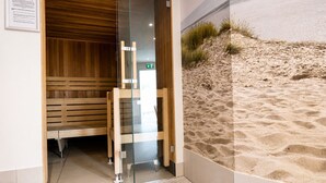 A sauna room with wooden benches and a glass door, a tiled floor, and a wall with a sand dune mural. - Vacation apartment Cuxhaven Döse on the beach | Lord Nelson No. 310 (Cuxhaven)