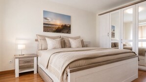 A bedroom with a bed, nightstands, a wardrobe, and a painting on the wall. - Vacation apartment Cuxhaven Döse on the beach | Lord Nelson No. 310 (Cuxhaven)