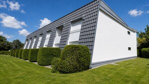 A modern building with a white exterior and grey roof tiles, surrounded by well-maintained green lawns and hedges.