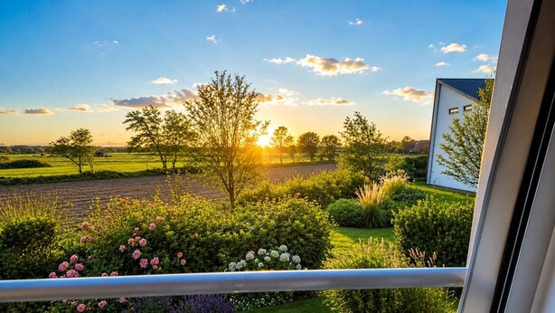 A balcony with a view of a garden and fields during sunset.