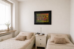 A bedroom with two beds, a nightstand, a framed abstract painting, and a window with a view. - Duhner Horizonte vacation apartment in Duhnen on the North Sea with loggia (Cuxhaven)