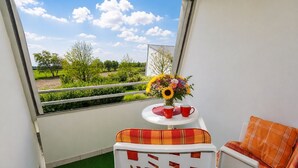 A balcony with a view of greenery and a table with a vase of flowers and two red cups.