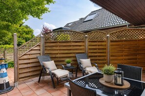 A patio with outdoor furniture, a wooden fence, and a small table with a plant. - Vacation apartment in Duhnen with terrace | StrandLiebe (Cuxhaven)