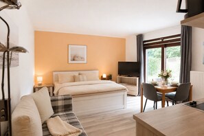 A hotel room with a bed, a sofa, a dining table with chairs, a TV, and a window with curtains. - Vacation apartment in Duhnen with terrace | StrandLiebe (Cuxhaven)