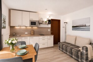 A compact living space with a kitchenette, dining area, and a sofa. - Vacation apartment in Duhnen with terrace | StrandLiebe (Cuxhaven)