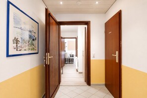 A hallway with a wooden door, a framed picture on the wall, and a tiled floor. - Vacation apartment in Duhnen with terrace | StrandLiebe (Cuxhaven)