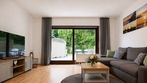 A modern living room with a television, sofa, coffee table, and a view of greenery outside.