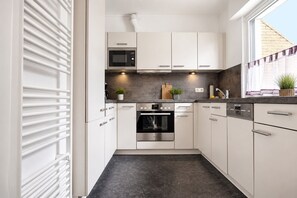 Una cocina moderna con gabinetes blancos, horno empotrado, microondas y lavavajillas.
