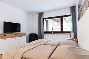 Un dormitorio con una cama, un televisor sobre un mueble, una ventana con cortinas y un radiador.