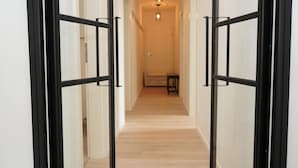 A hallway with a wooden floor and black-framed glass doors leading to a room.